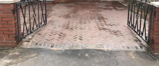 Red block paved driveway in a herringbone pattern after cleaning, seen through open iron gates