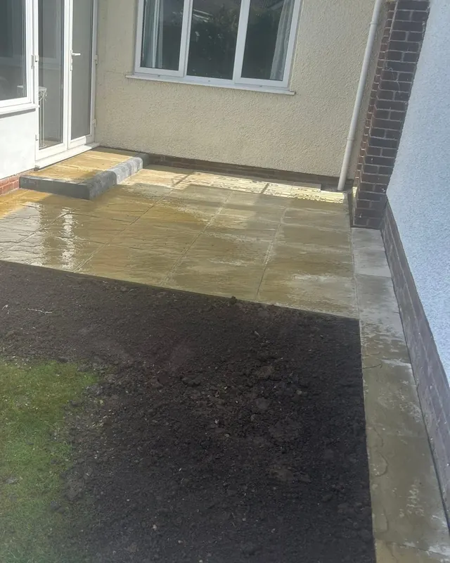 New buff patio and grey step outside a conservatory, with fresh topsoil graded beside the lawn