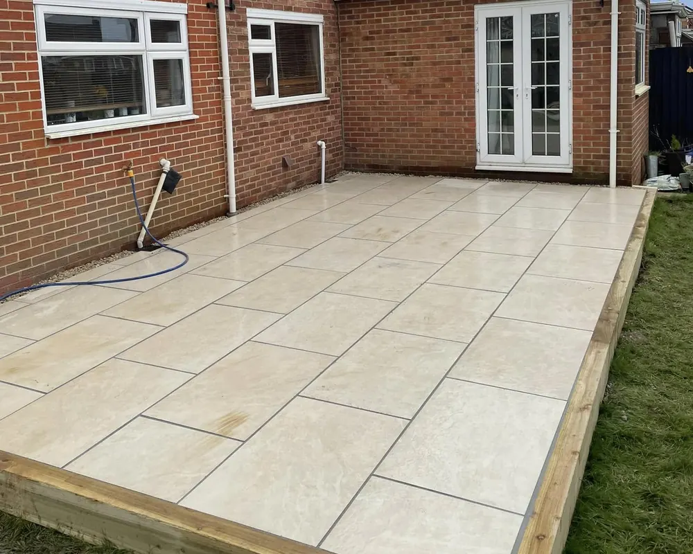 Cream porcelain patio with a timber sleeper edge, laid behind a red brick house