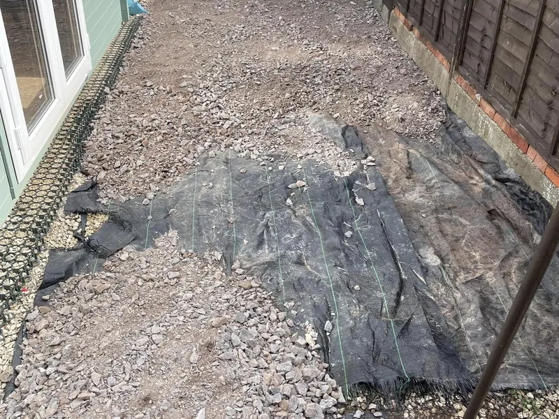 Garden beside a green garden room dug out to bare ground, with weed membrane and loose stone