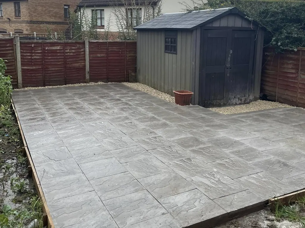 Large grey paved area with a timber edge and a gravel border, laid beside a garden shed